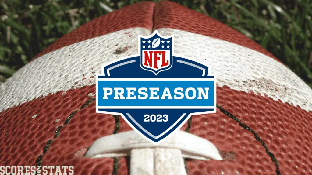 Close-up of a worn NFL football with a blue "PRESEASON 2023" logo, set against a grassy background.