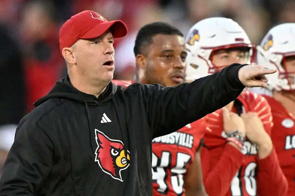 Louisville football coach gestures and gives instructions from the sideline during a game.