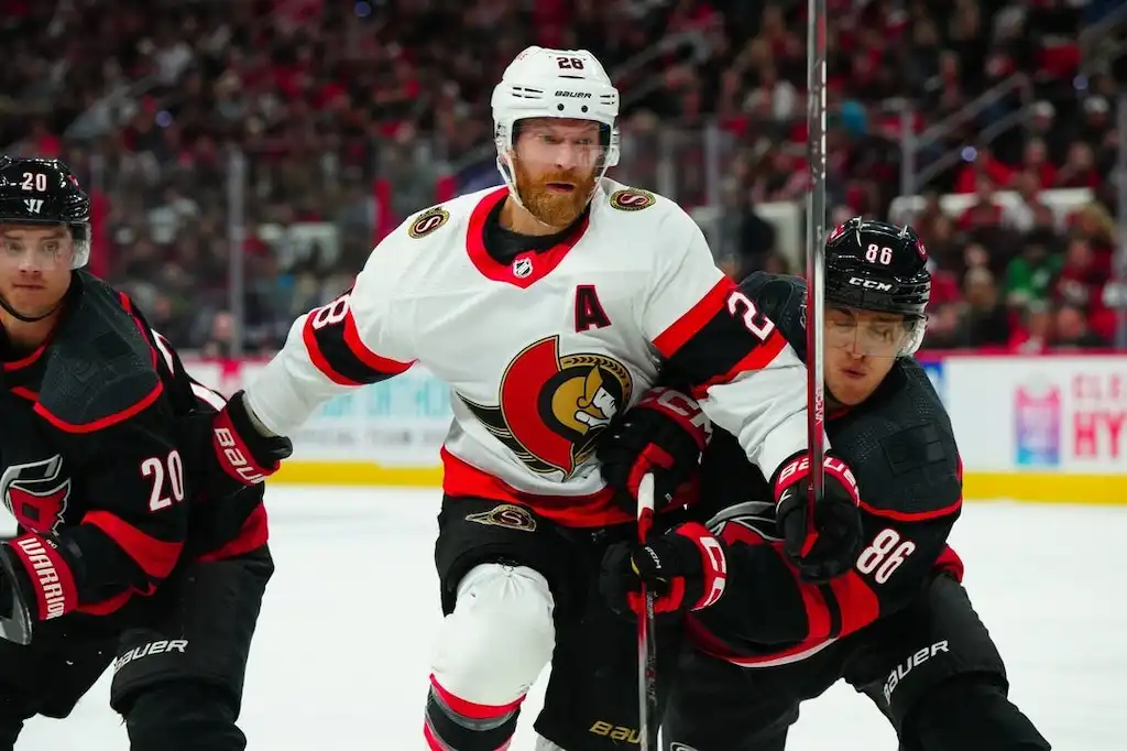 Ottawa Senators player battles for position against two defenders during an NHL game.