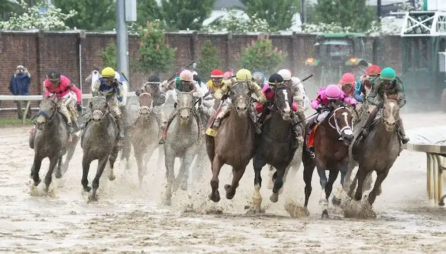 Horses race around a muddy track, kicking up dirt as jockeys guide them through a turn.