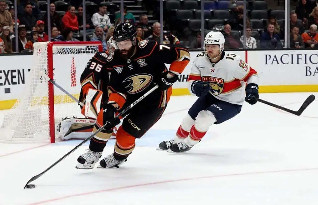 Anaheim Ducks defenseman skates behind the net with the puck while being chased by a Florida Panthers forward.