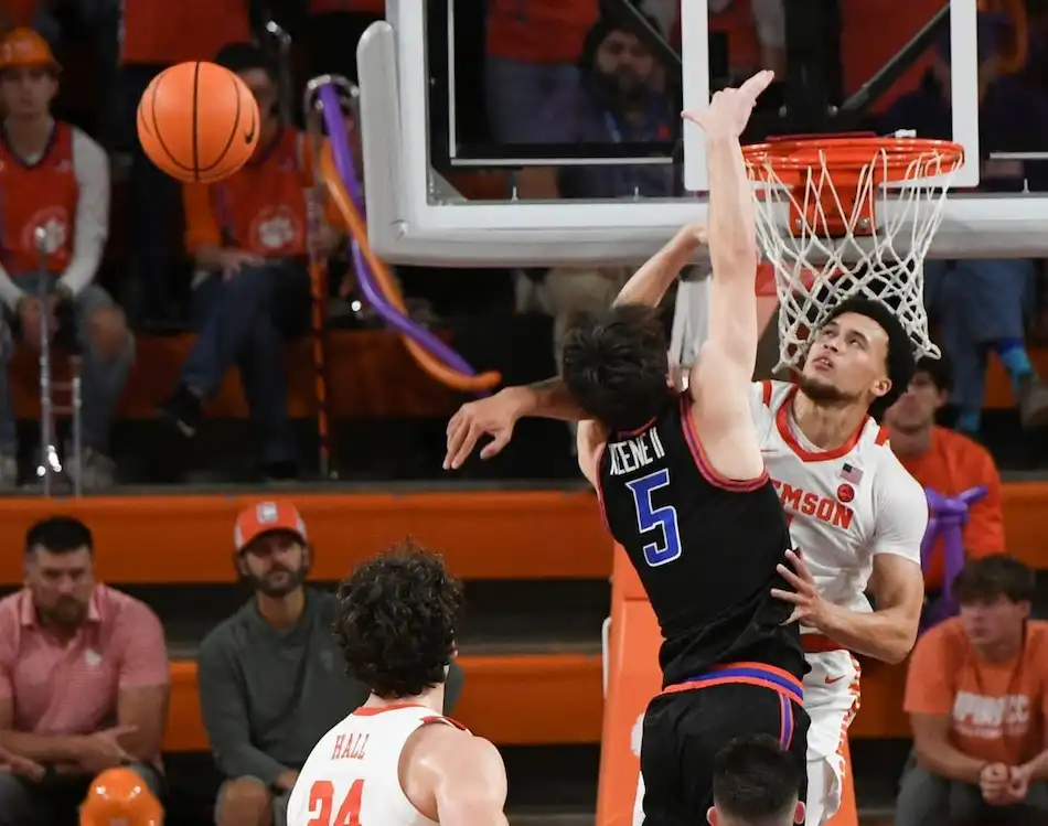 Clemson basketball player leaps to block a shot at the rim by an opposing player