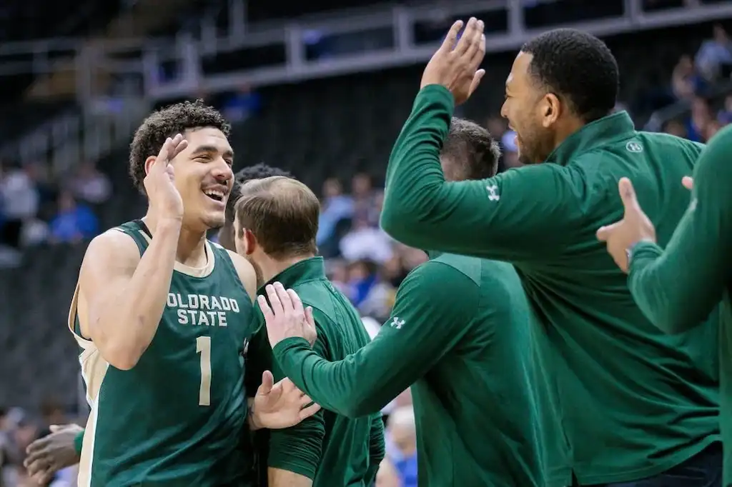 NCAAB 3 Colorado State player celebrates with teammates and coaches on the sideline.
