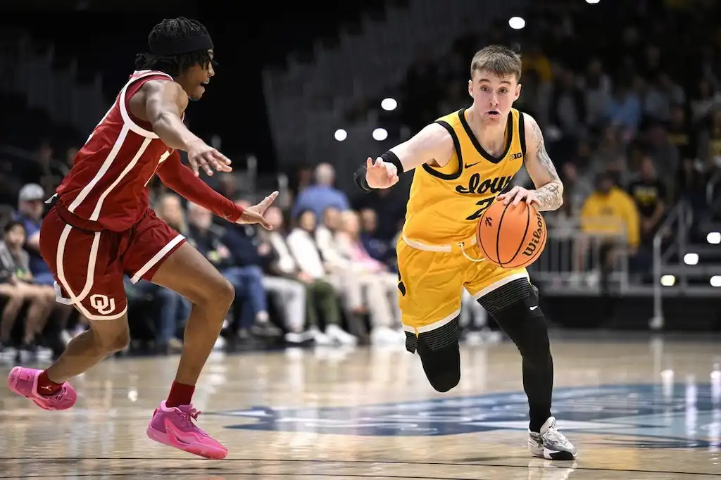A Iowa basketball player dribbles up the court while being closely guarded by a defender.