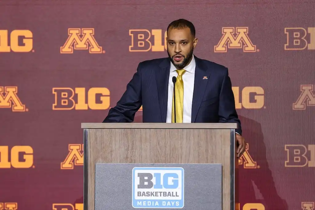 A Minnesota Golden Gophers basketball coach speaks at the podium.