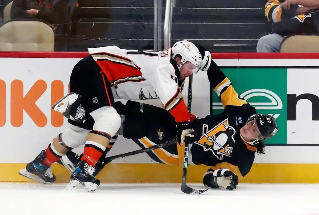 Anaheim Ducks player checks a Pittsburgh Penguins player into the boards during an NHL game.