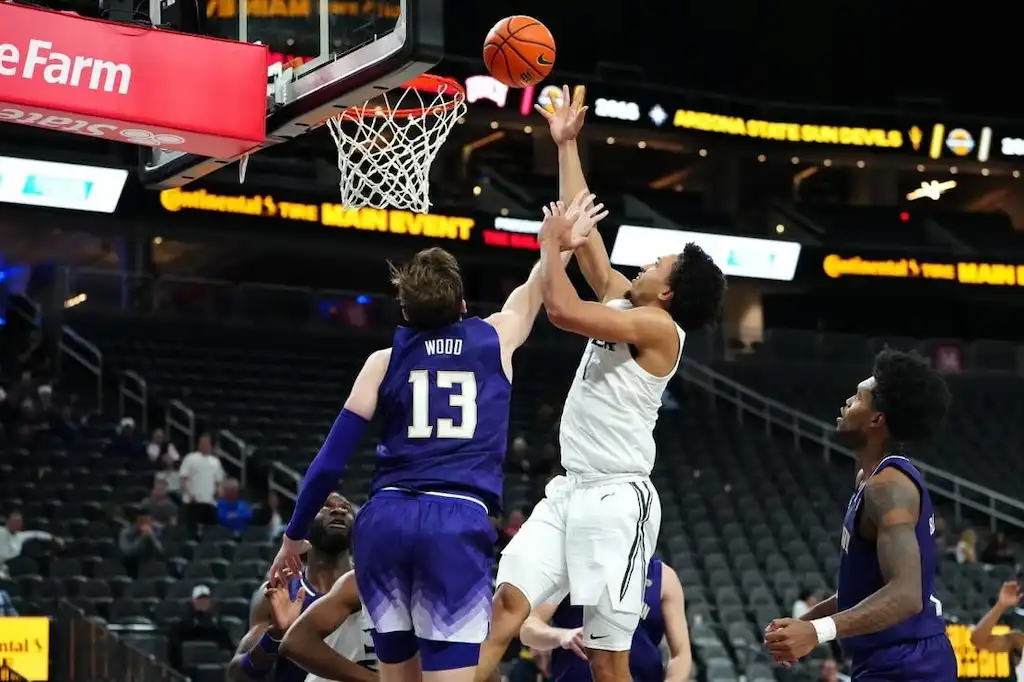 A college basketball player goes up for a layup while being defended by an opposing player.