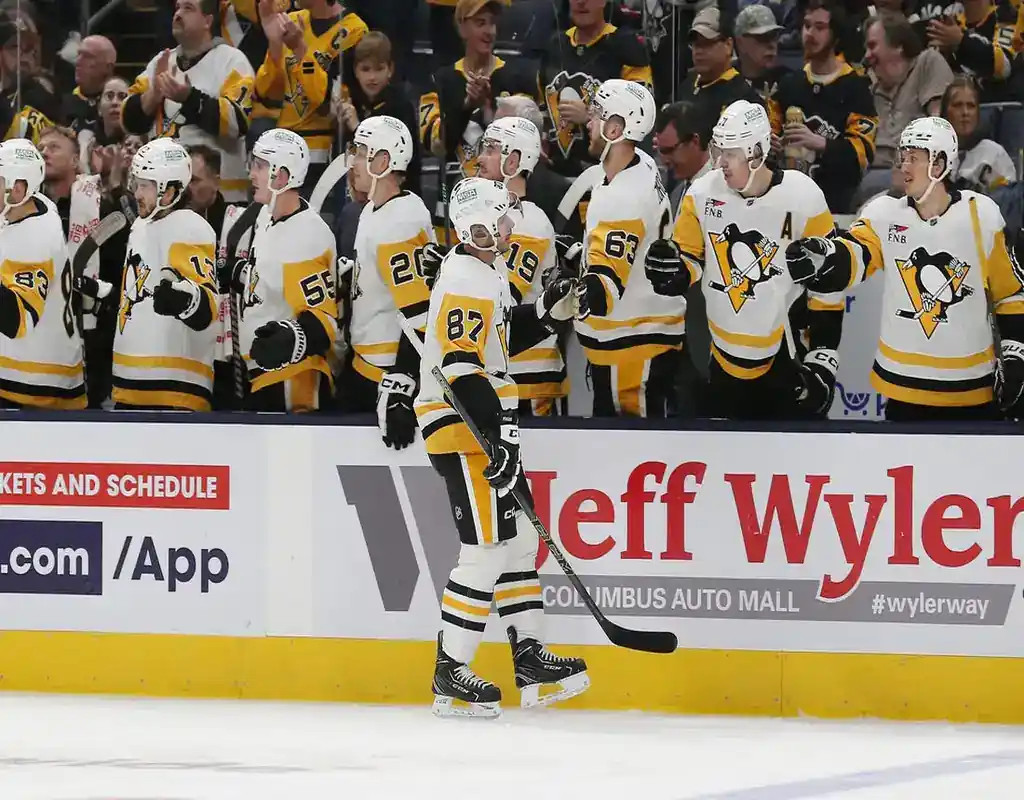 Pittsburgh Penguins players celebrate at the bench during an NHL game, with Sidney Crosby leading the moment in May 2025.