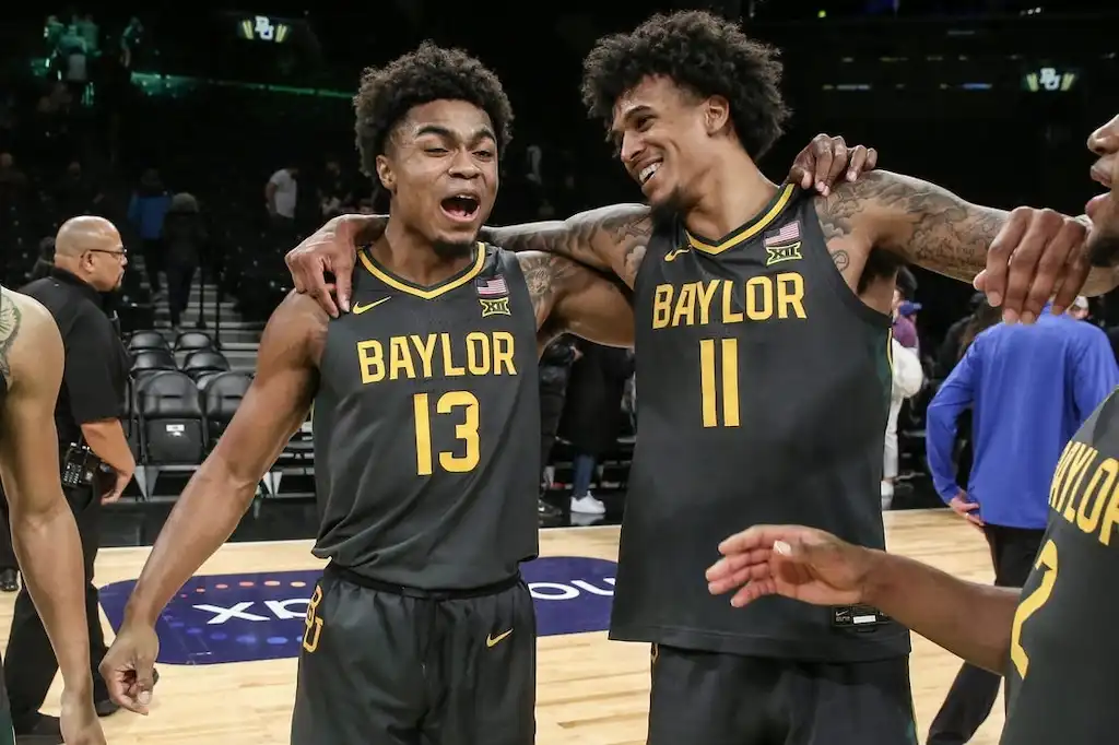 NCAAB 5 Two Baylor basketball players, smile and celebrate together on the court after a game.