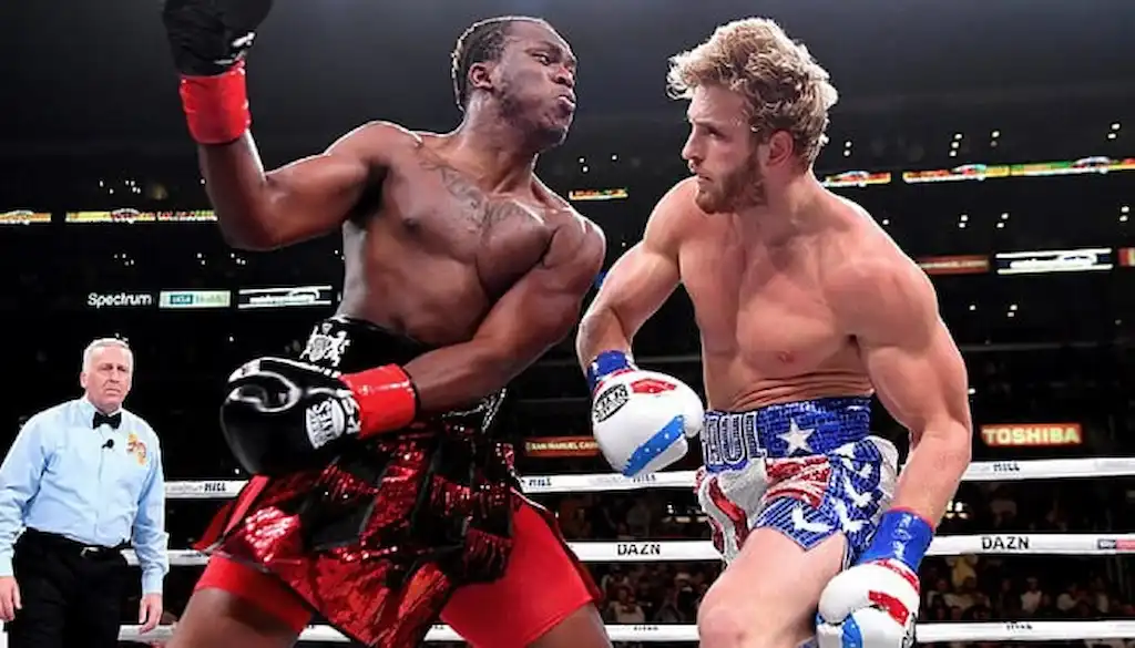 Two boxers exchange powerful punches in the middle of a high-intensity match inside a brightly lit arena.