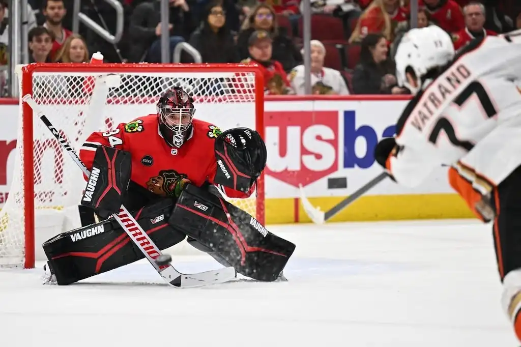 Chicago Blackhawks goalie crouches in front of the net, ready to block a shot from an Anaheim Ducks player.