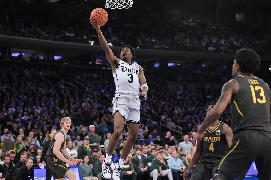 NCAAB 1 A Duke basketball player goes up for a layup while being challenged by multiple defenders.