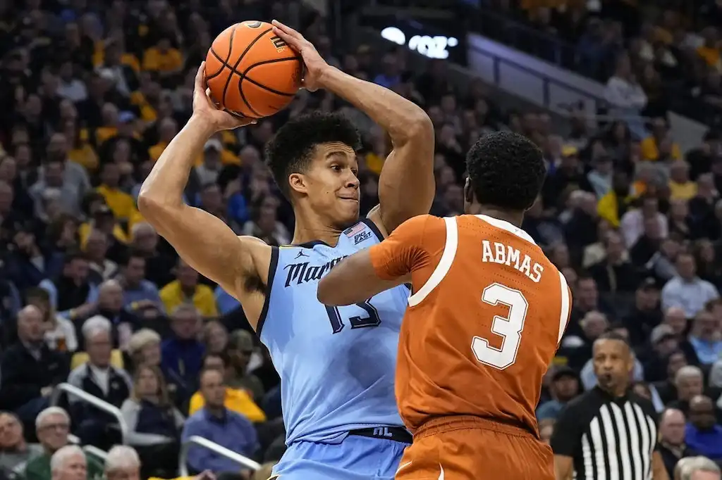 A Marquette player holds the ball above his head while being tightly defended by Texas guard.