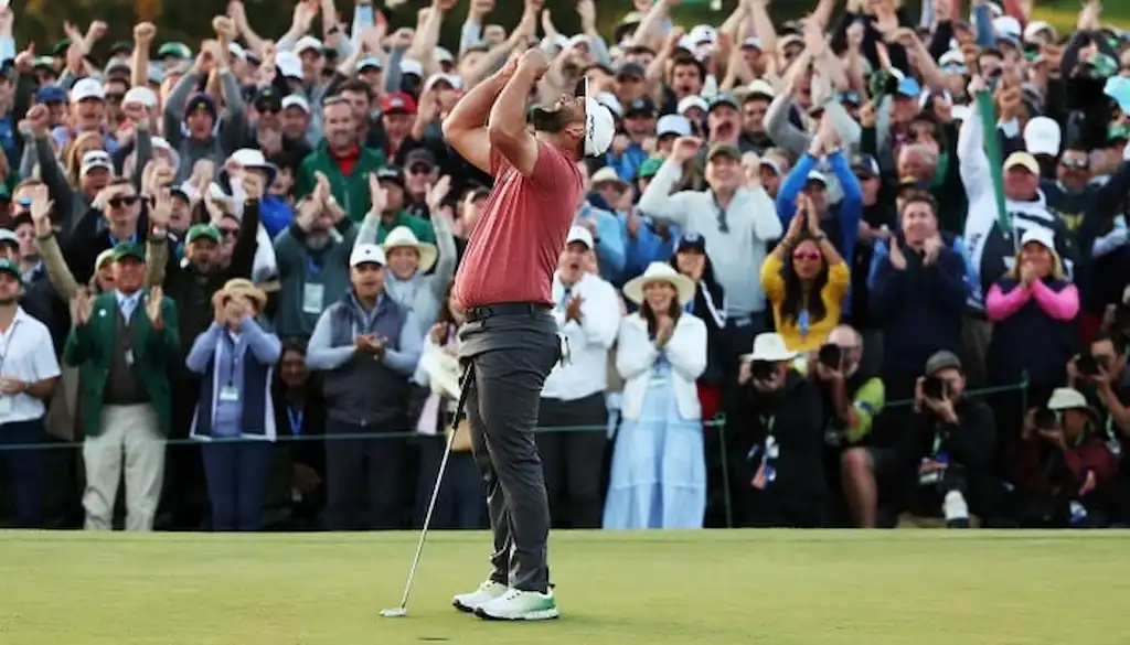 A golfer in a red shirt celebrates emotionally on the green after sinking a putt.
