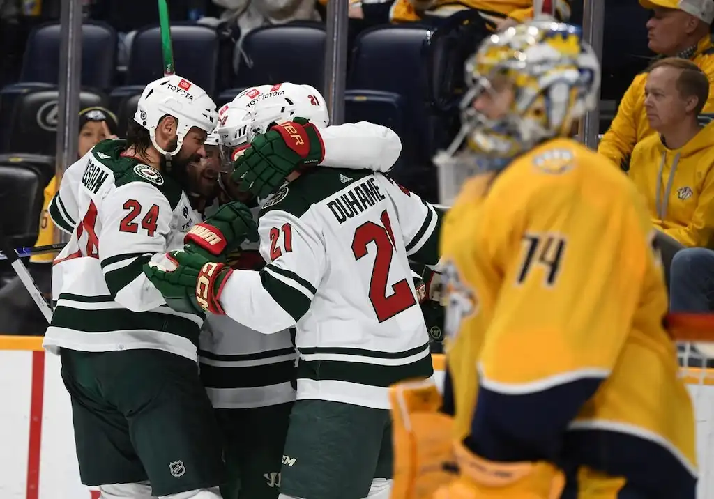 Minnesota Wild players celebrate a goal by hugging near the boards during an NHL game.