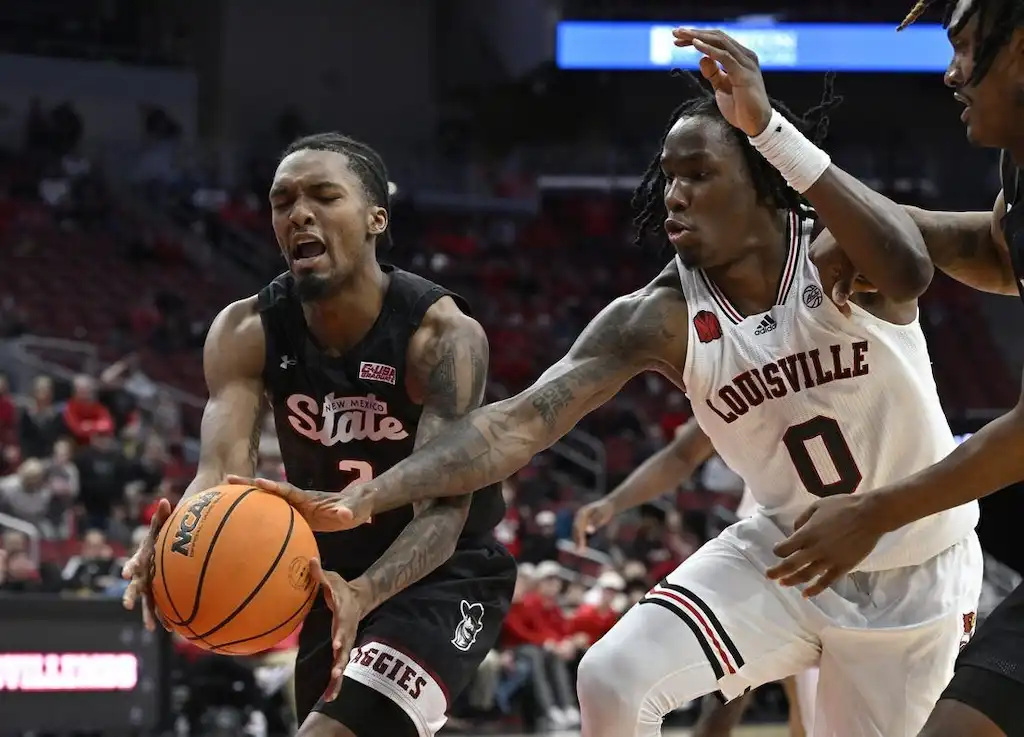 NCAAB 8 New Mexico State basketball player battles for possession of the ball with a Louisville player.