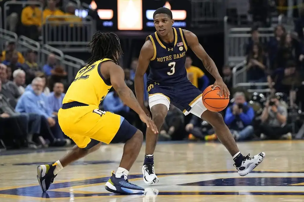 A Notre Dame basketball player dribbles the ball while sizing up a defender from Marquette.