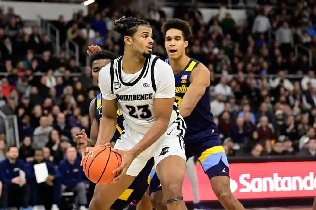 Providence Friars basketball player holds the ball while being closely guarded by Marquette players.