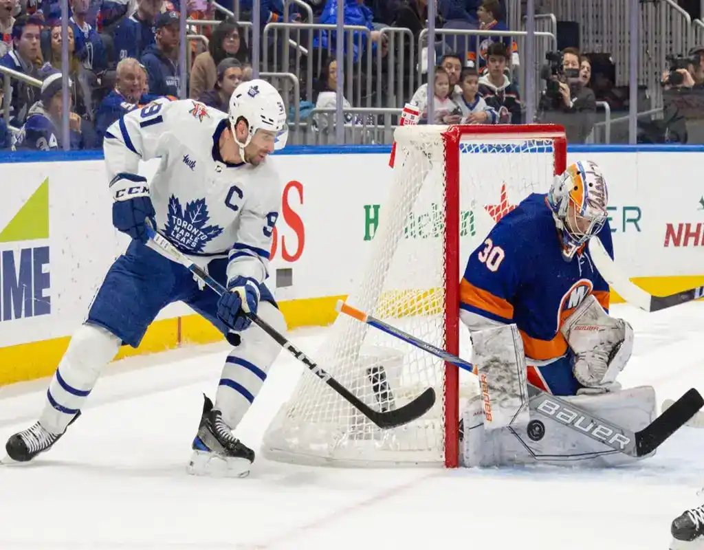 Toronto Maple Leafs forward controls the puck behind the net while New York Islanders goalie defends