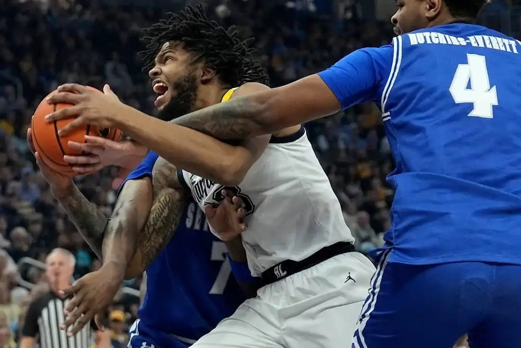 NCAAB 6 Marquette Golden Eagles player drives to the basket while being defended by two players.