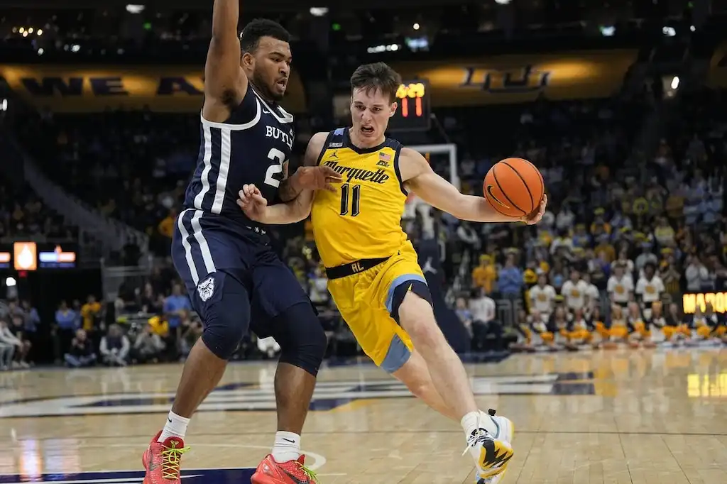 A Marquette basketball player drives to the basket while being closely guarded by a defender.