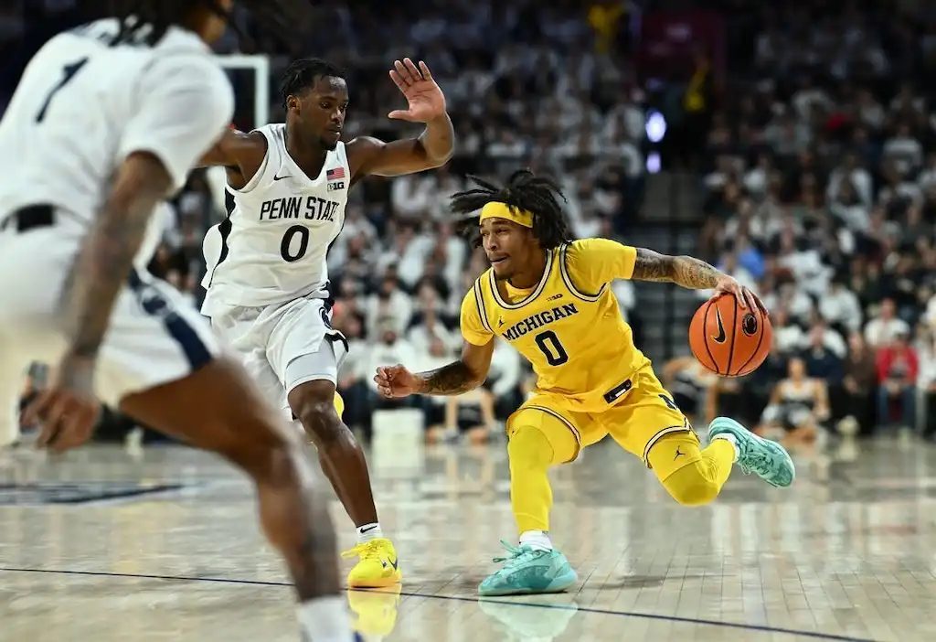 A Michigan basketball player dribbles quickly past a Penn State defender.