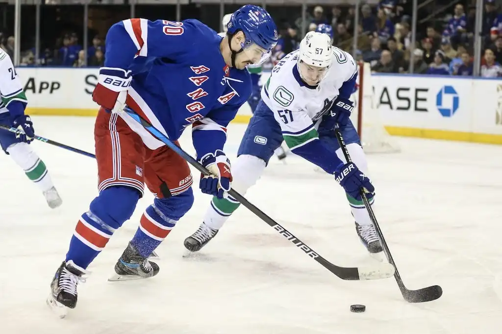 NHL 3 A New York Rangers player and an opposing player battle for the puck during a game.