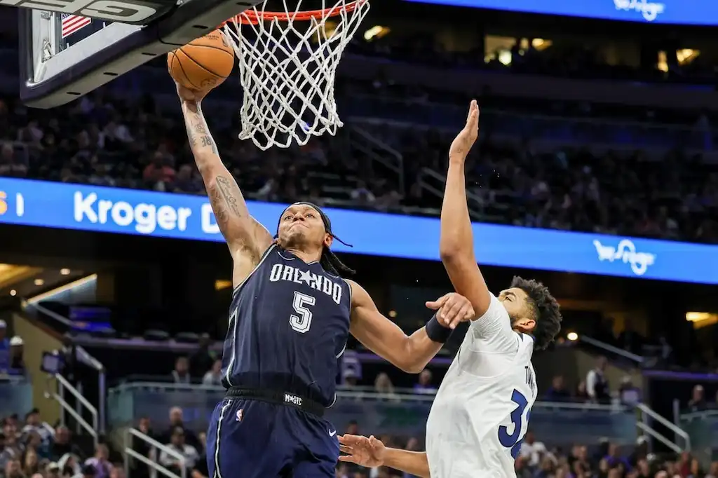 An Orlando Magic player soars toward the basket for a powerful one-handed dunk.
