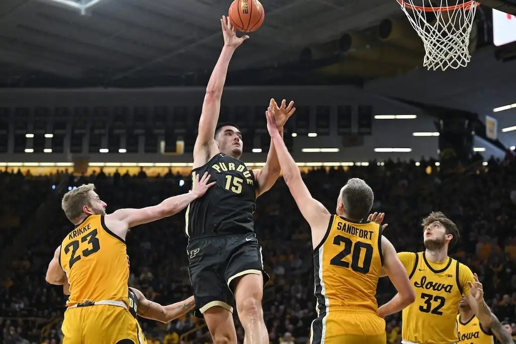 Purdue Boilermakers player goes up for a one-handed shot over Iowa Hawkeyes defenders.