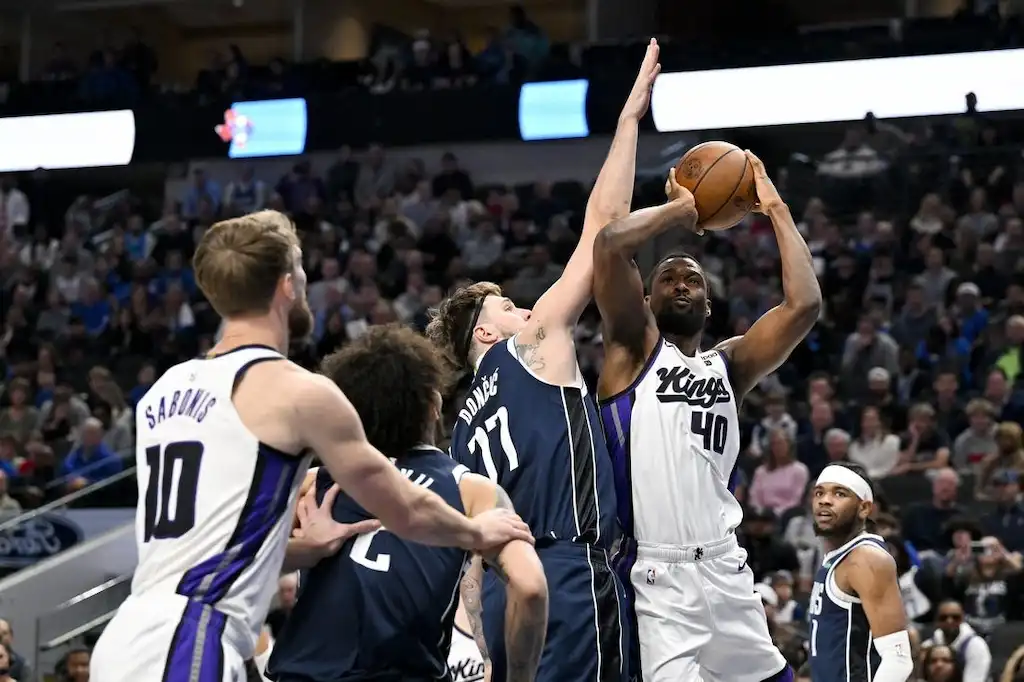 A Sacramento Kings player goes up for a shot while being tightly defended by a Dallas Mavericks player.