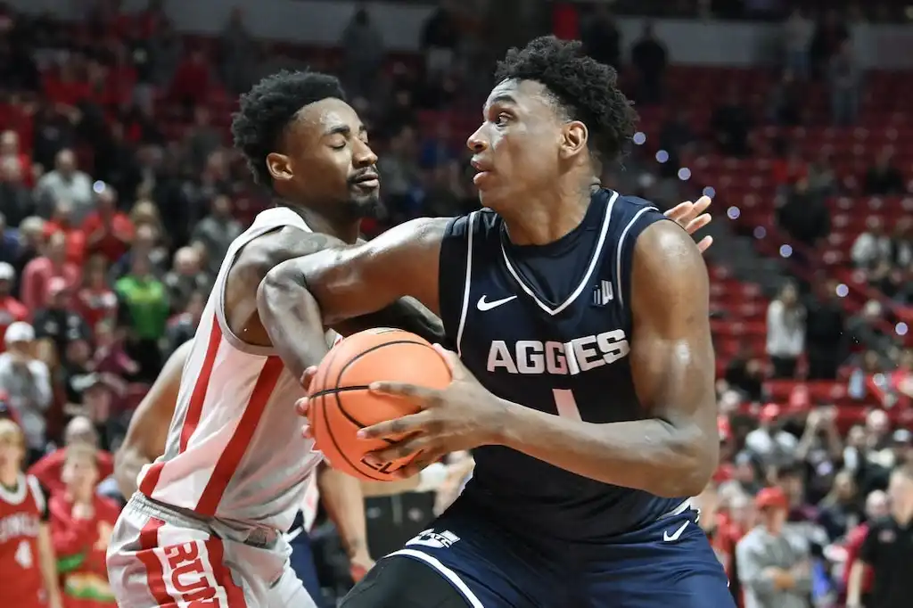 A Utah State Aggies player drives to the basket while being tightly defended by a player.