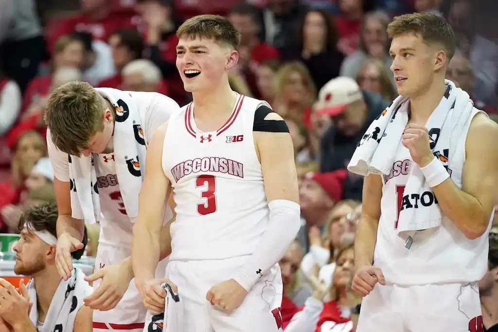 Wisconsin basketball players cheer from the bench with energy and excitement.