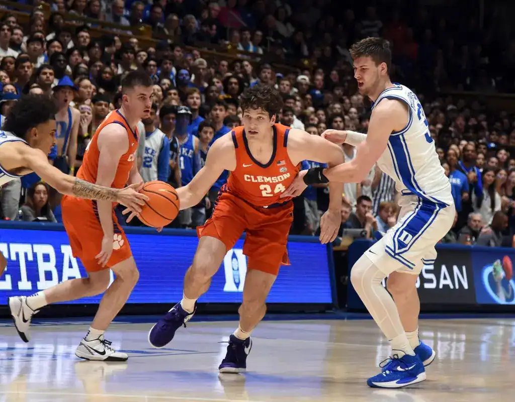 Clemson Tigers #24 driving toward the basket as Louisville Cardinals defender contests the play in a full arena