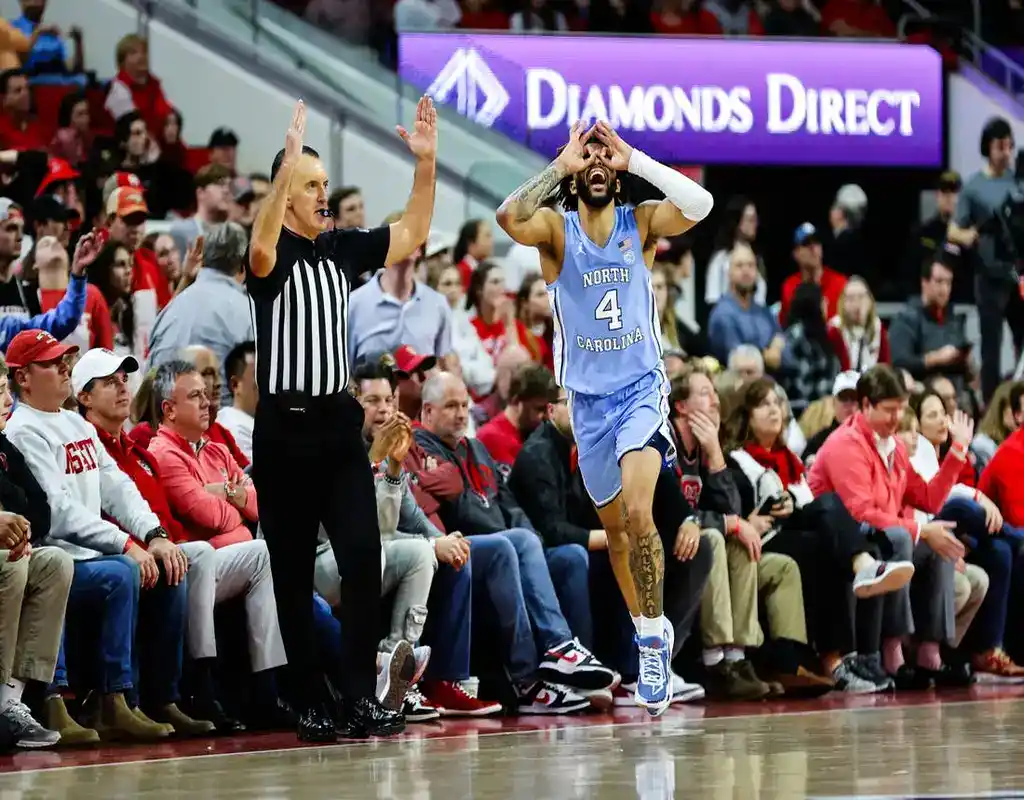 “North Carolina Tar Heels player #4 appealing to a referee’s call during a game against the Syracuse Orange at a packed arena.”