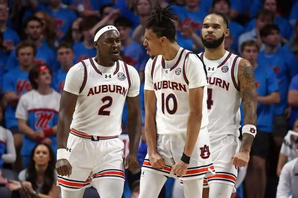 Three Auburn Tigers basketball players in an intense moment—clearly hyped up and feeding off the energy of a big play.