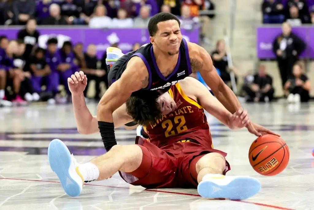NCAAB 9 A Iowa State basketball player sits on the floor while an opposing player crashes into him during a scramble for the ball.