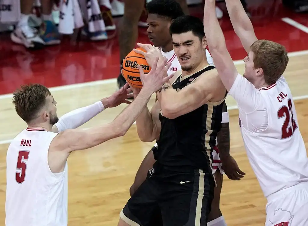 A Purdue player holds the ball tightly while being double-teamed by two defenders.