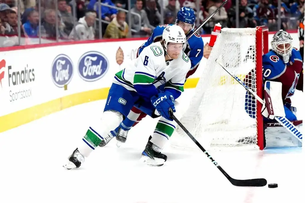 NHL 7 Vancouver Canucks player controls the puck behind the net while being closely pursued by a Colorado Avalanche defender.