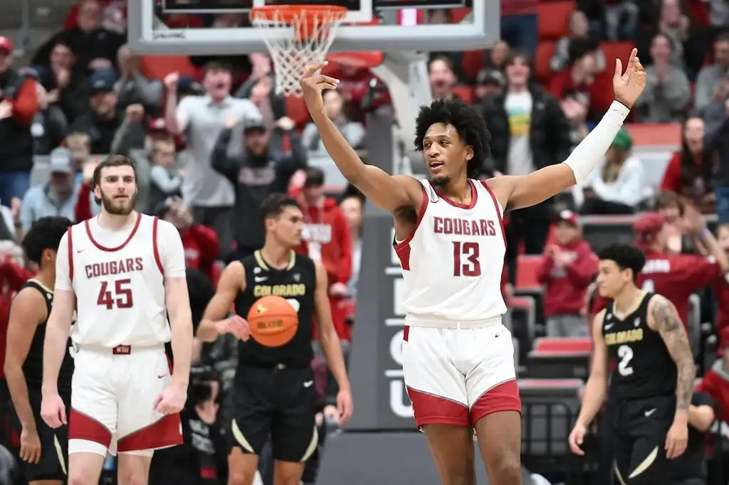 A Washington State basketball player raises his arms in celebration.