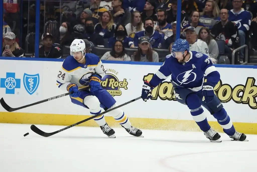 A Buffalo Sabres player controls the puck while being chased by a Tampa Bay Lightning player.