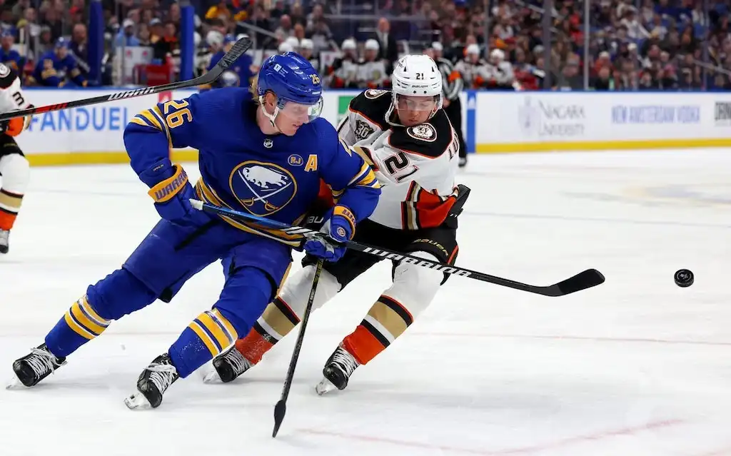 A Buffalo Sabres player shields the puck from a defender while skating up the ice.