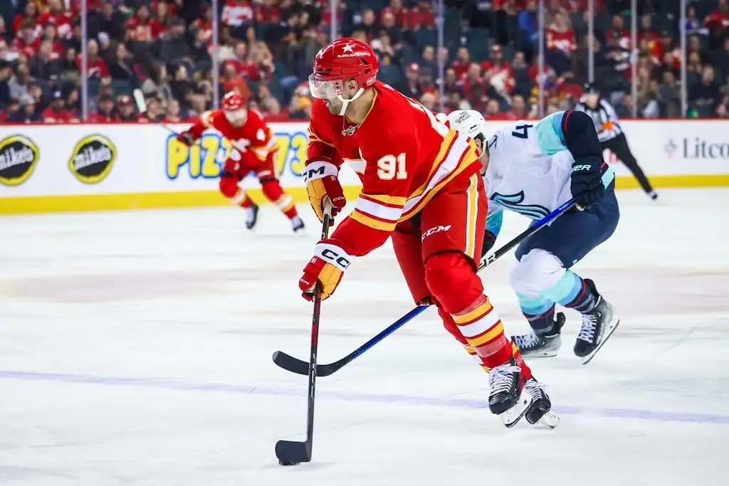 Calgary Flames player controls the puck while skating past a defender.