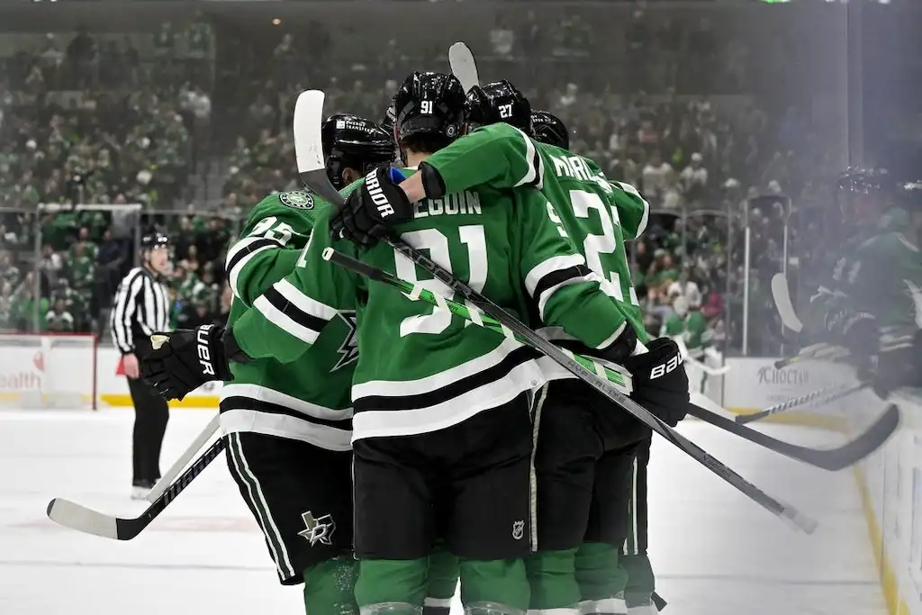 Dallas Stars players celebrate a goal with a group hug on the ice.