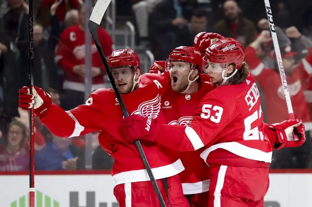 Three Detroit Red Wings players celebrate a goal on the ice.