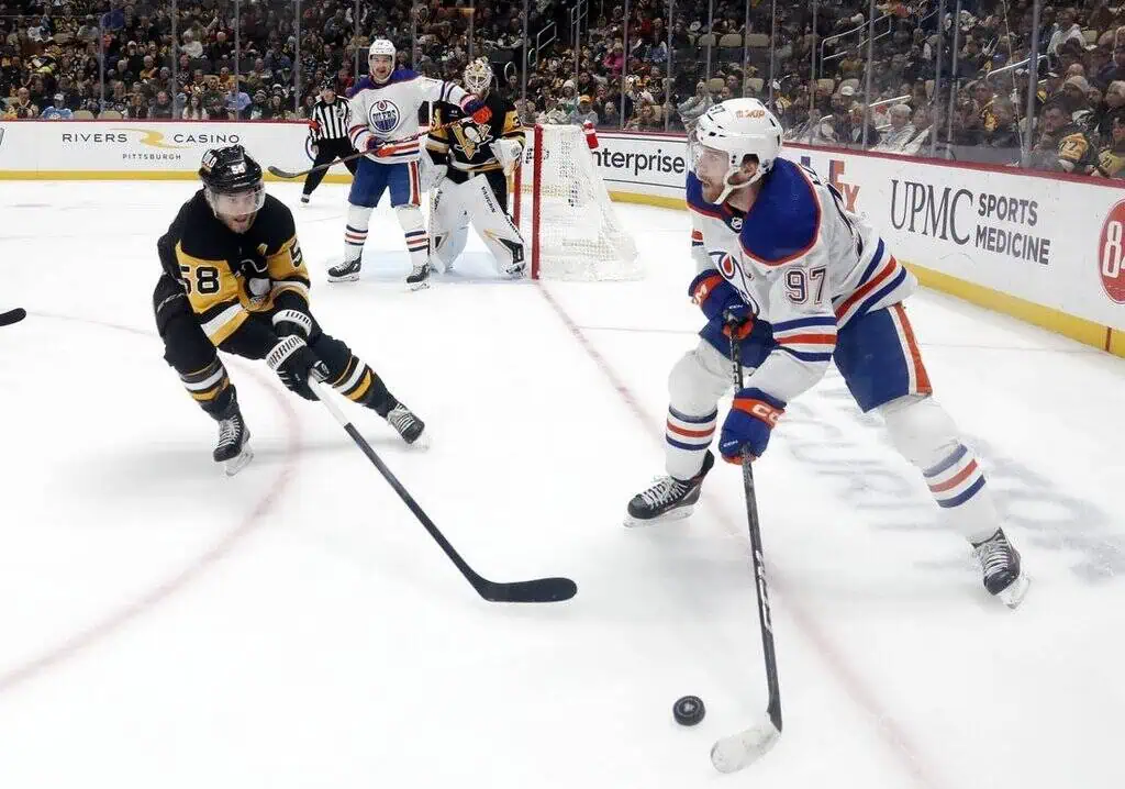 A player from the Edmonton Oilers (#97) controlling the puck while being closely defended by a Pittsburgh Penguins player (#58).