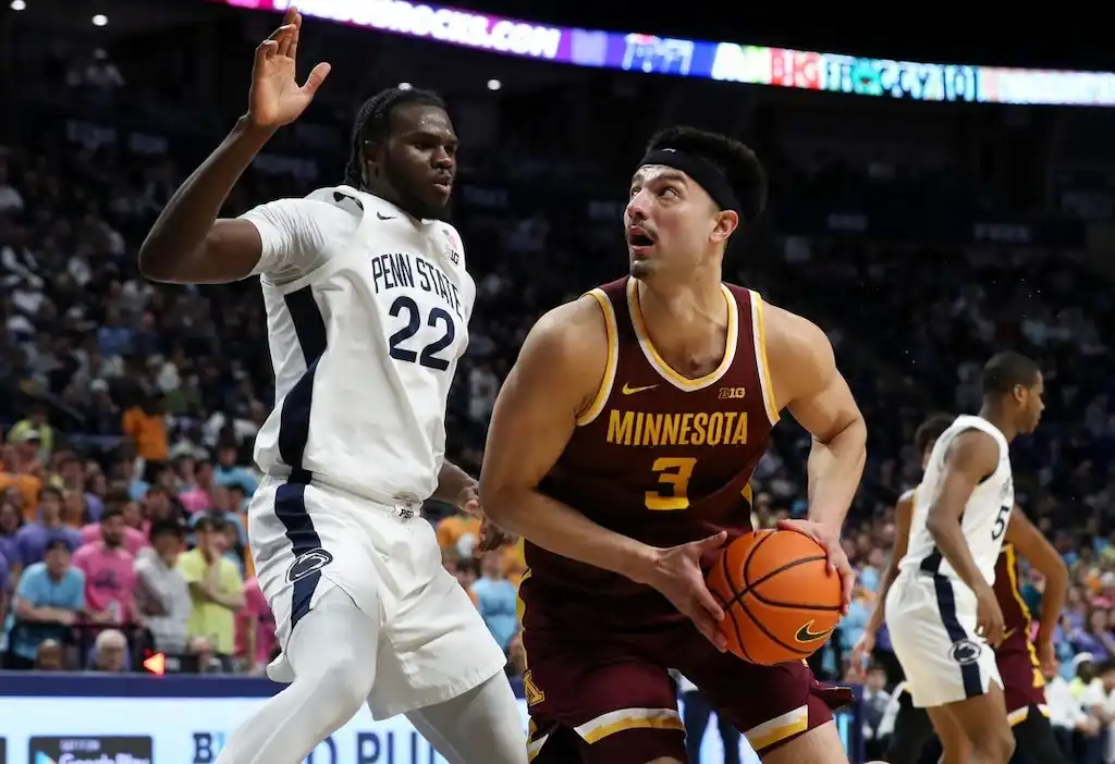 A Minnesota Golden Gophers basketball player drives toward the basket while closely guarded by a defender.