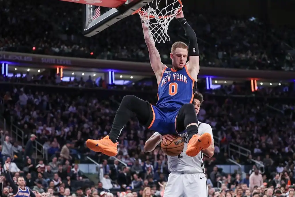 A New York player hangs from the rim after finishing a powerful dunk during an NBA game.