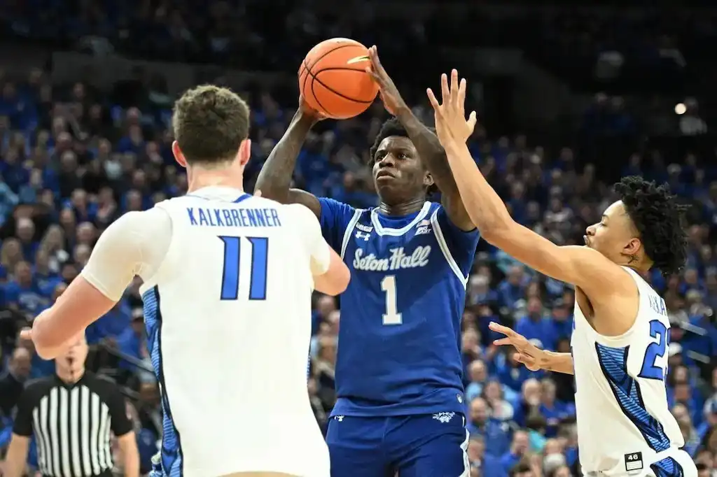 NCAAB 5 Seton Hall player attempts a jump shot while being defended by two players.