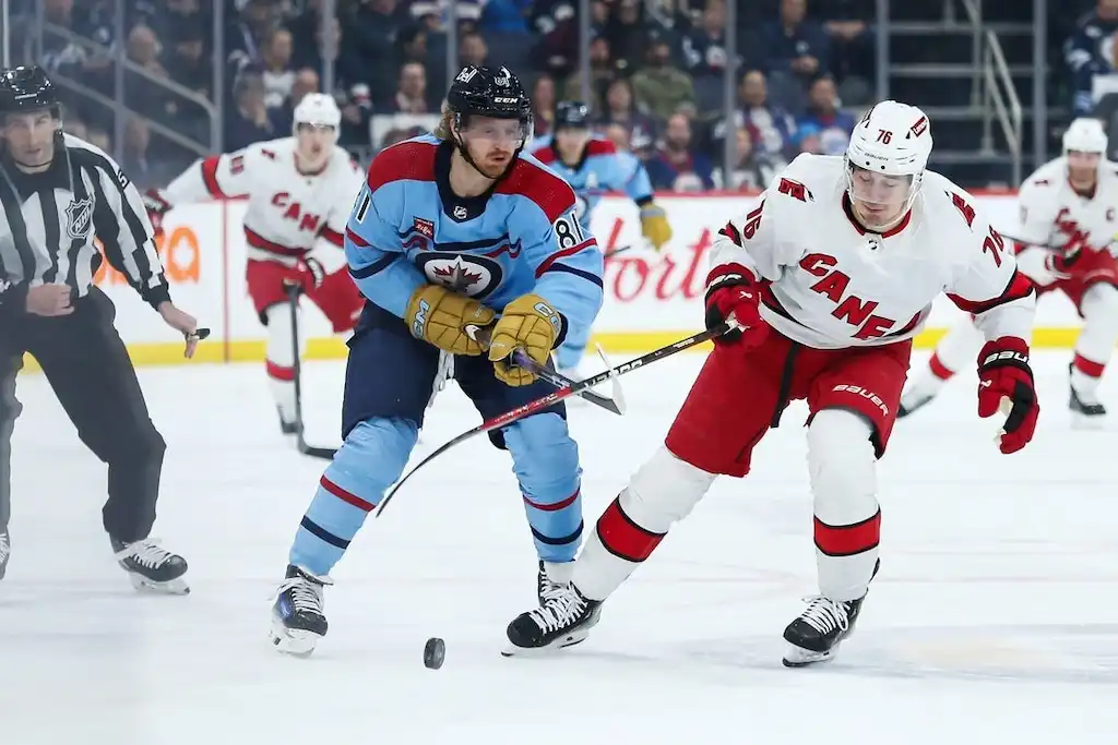 Winnipeg Jets player and Carolina Hurricanes player battle for the puck during an NHL game.