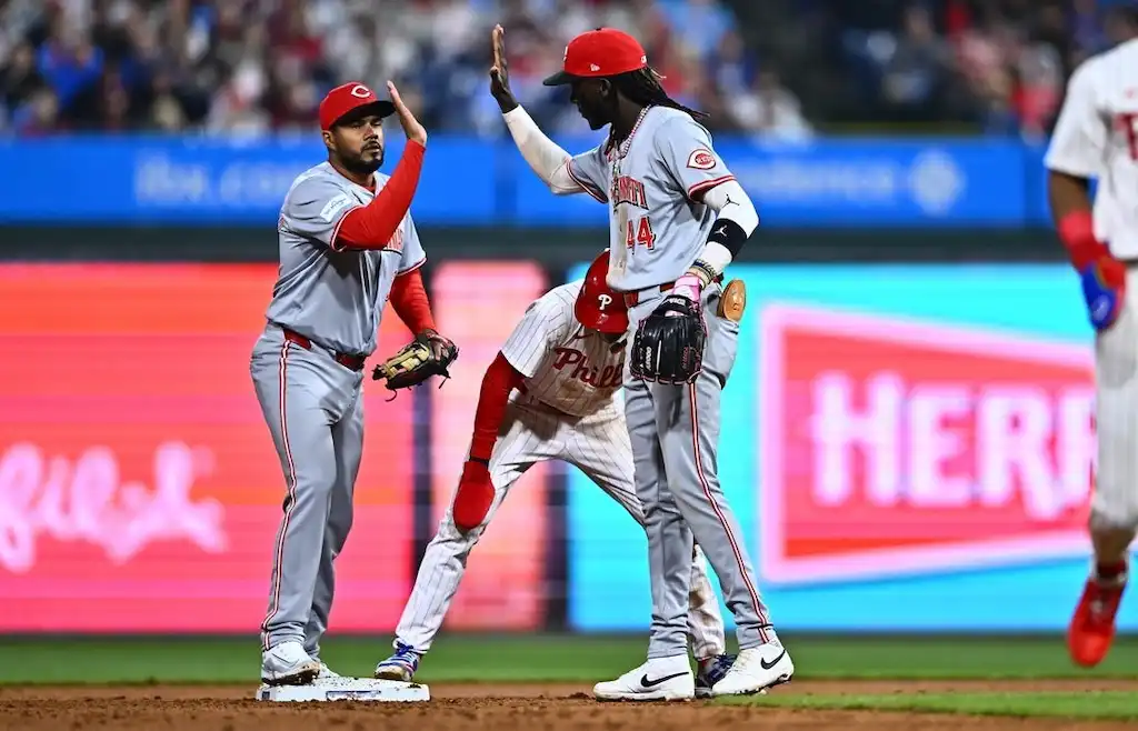 Two Cincinnati Reds players in gray uniforms celebrate with a high five after a defensive play at second base.
